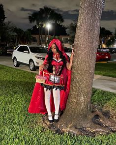 a woman dressed as a red riding hood leaning against a tree