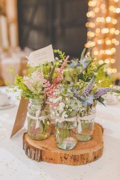 three mason jars filled with flowers sitting on top of a wooden coaster at a wedding reception