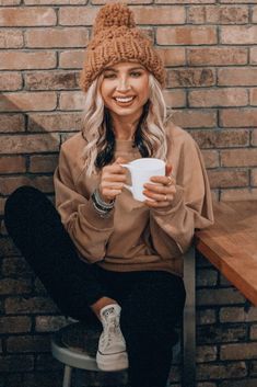 a woman sitting on top of a wooden bench holding a white cup in her hands