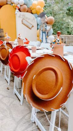 several hats are lined up on tables with balloons in the shape of animals behind them