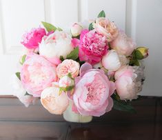 a vase filled with pink and white flowers on top of a wooden floor next to a door