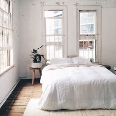 a bed sitting in a bedroom next to two windows and a rug on the floor