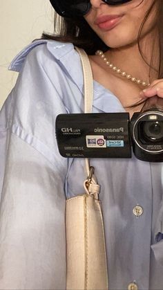 a woman holding a camera in her right hand and wearing sunglasses on top of her head