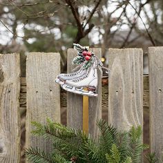 an ice skate decoration sitting on top of a wooden fence next to a pine tree