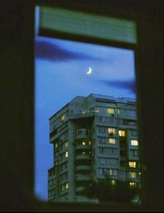 the moon is seen through an open window in a building at night with lights on