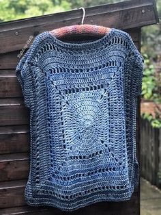 a blue crocheted sweater hanging on a wooden fence