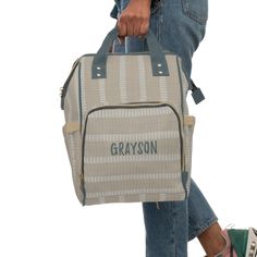 a person carrying a gray and white bag with the word greyson on it's side