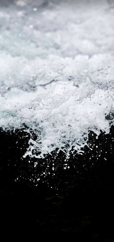 the water is splashing on top of the black foamy ocean wave with white bubbles