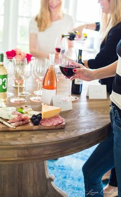 two women standing at a table with wine and cheese