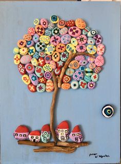 a tree with colorful buttons on it sitting in front of a blue wall and two little houses