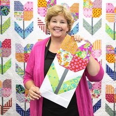 a woman holding up a piece of art made out of paper and fabric, in front of a quilted wall