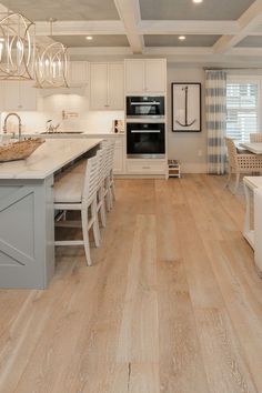 a large kitchen with white cabinets and wood flooring is pictured in this image, there are several chandeliers hanging from the ceiling