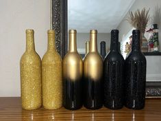 five bottles are lined up on a table in front of a mirror, and one is gold