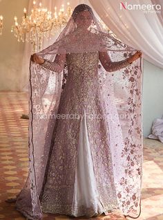 a woman in a purple and white dress with a veil over her head, standing next to a chandelier