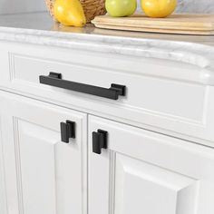 two apples and some lemons on a counter in a kitchen with white cabinets, black handles