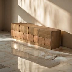 a wooden bench sitting in the middle of a room next to a window with sunlight streaming through it