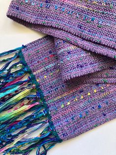 a purple scarf with multicolored beads and fringes on it sitting on top of a white surface