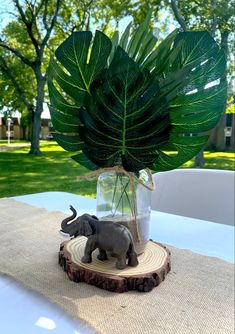 an elephant figurine sitting on top of a piece of wood next to a plant