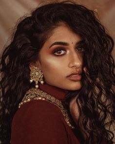 a woman with long dark hair and brown eyeshadow wearing gold jewelry, posing for the camera