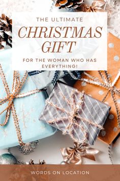 A festive image of wrapped Christmas gifts with the text "THE ULTIMATE CHRISTMAS GIFT FOR THE WOMAN WHO HAS EVERYTHING!" overlaid. The gifts are wrapped in various colors including blue, grey, and orange, with sparkly ribbons and decorations. Pine cones and ornaments are visible in the background. The image has a warm, cozy holiday feel with a color palette of soft blues, oranges, and metallics. "WORDS ON LOCATION" is written at the bottom of the image. Christmas Host Gift, Sustainable Christmas Gifts, Eco Friendly Christmas Gifts, Meaningful Christmas, Sustainable Christmas, Preschool Gifts, Christmas Gift List, Host Gifts, Kids Birthday Gifts