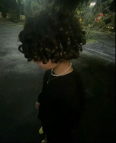 a woman with curly hair standing in the street at night wearing a black shirt and pearls necklace