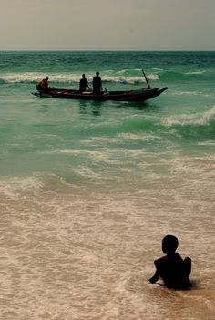 two people in a small boat on the ocean with one person sitting and another standing