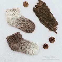 two pairs of knitted slippers next to pine cones and a piece of wood