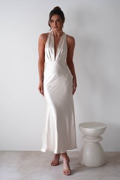 a woman in a white dress standing next to a vase and chair with her hands on her hips