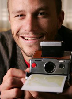 a smiling man holding an old fashioned camera