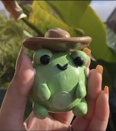 a hand holding a green toy with a hat on it's head and eyes