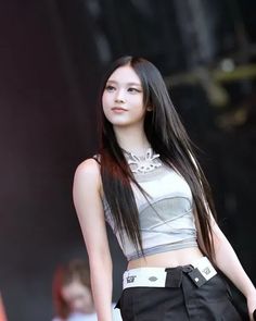 a woman with long black hair standing in front of a microphone and wearing a skirt