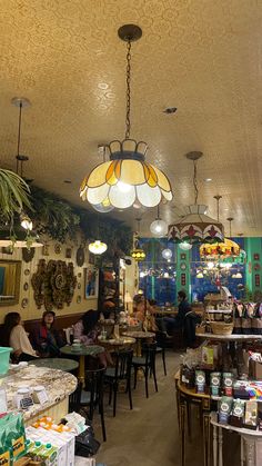 people sitting at tables in a restaurant with lamps hanging from the ceiling and windows above them