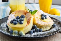 two pancakes with blueberries and powdered sugar are on a plate next to orange juice