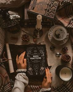 a person sitting at a table reading a book with candles and other items around it