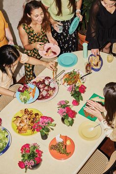 a group of women standing around a table with plates of food on it and flowers in vases