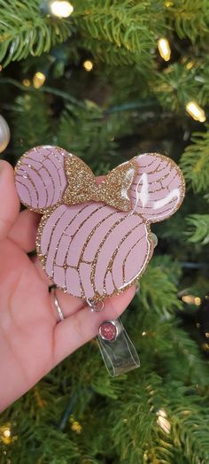 a hand holding a pink and gold minnie mouse brooch in front of a christmas tree