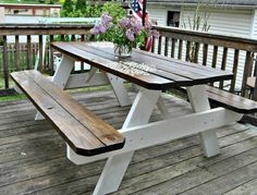 a wooden picnic table on a deck with purple flowers in a vase next to it