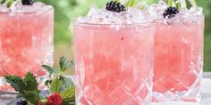 three glasses filled with ice and berries on top of a wooden table in front of trees