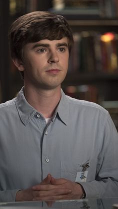 a young man sitting at a table in front of a book shelf with books on it