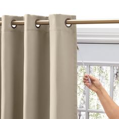 a woman is opening the curtains with her hand and pointing at it in front of a window