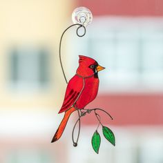 a red bird sitting on top of a window sill next to a green branch