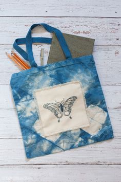 a tote bag with a butterfly on it and pencils in the pocket next to it