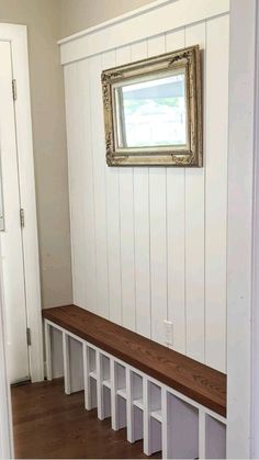 a wooden bench sitting in front of a white wall with a framed picture on it