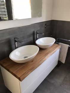 two white bowls sit on top of a wooden counter in a gray and white bathroom