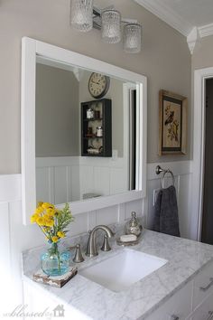 a bathroom with a sink, mirror and yellow flowers in a vase on the counter