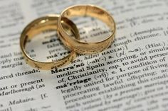 two gold wedding rings sitting on top of an open bible with the word marriage written in it