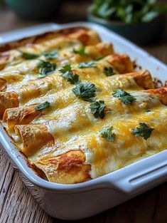 a casserole dish with cheese and green garnish on the top, sitting on a wooden table