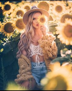 a woman wearing a hat and holding a teddy bear in front of a field of sunflowers