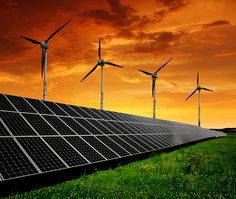 several wind turbines and solar panels in the grass at sunset with red sky behind them