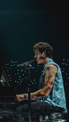 a man sitting at a piano on stage with headphones in his ears and one hand holding a microphone